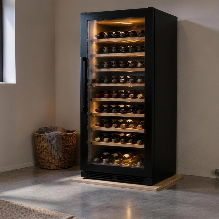Zwarte vrijstaande wijnkoelkast met verlichte glasdeur op een houten onderlegger in een bijkeuken naast een garagedeur